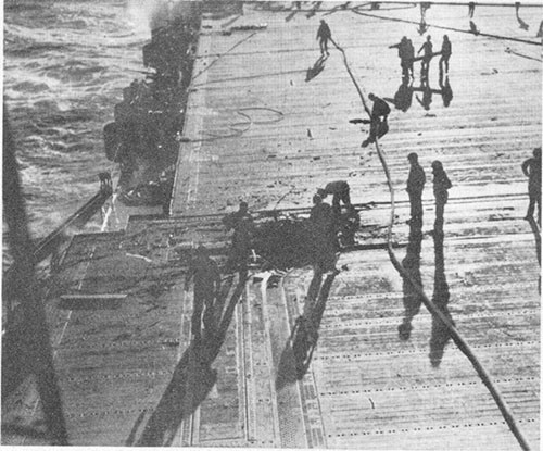 Photo E-17: Third hit. View of flight deck showing bomb hole near after starboard corner of No. 2 elevator.
