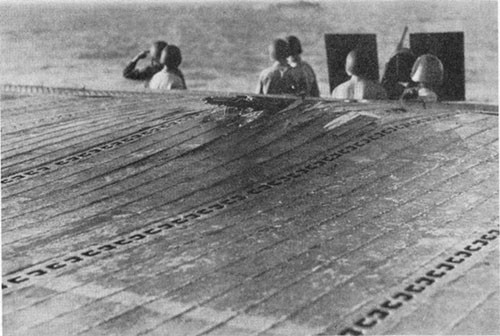 Photo E-20: Near-miss. Damage to extreme after port corner of flight deck caused by water column from the near-miss.