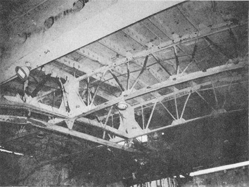 Photo J-9: Overhead of hangar deck looking forward and to port showing bulge in flight deck frames 58 to 26. Note buckling of girder struts in bents at frames 46 and 50.