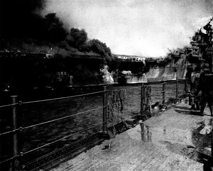 Photo 16: 19 March Action. Distant shot of fire in after part of Franklin. Burning gasoline is still pouring out of roller door opening about frame 170. Note men at stern escaping via net.