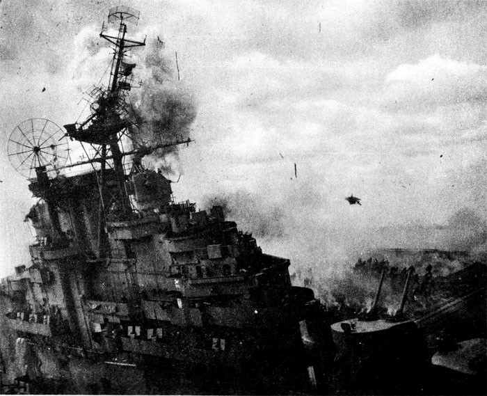 Photo 14: 19 March Action. Picture taken at the instant of a high order detonation on port side. Note debris in air and firefighters running to escape. Note topmast broken at radar platform level.