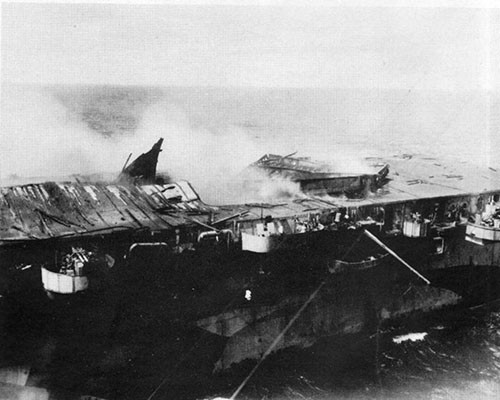 View of damage to after end of flight deck as a result of explosions in hangar. Note overturned elevator platform.