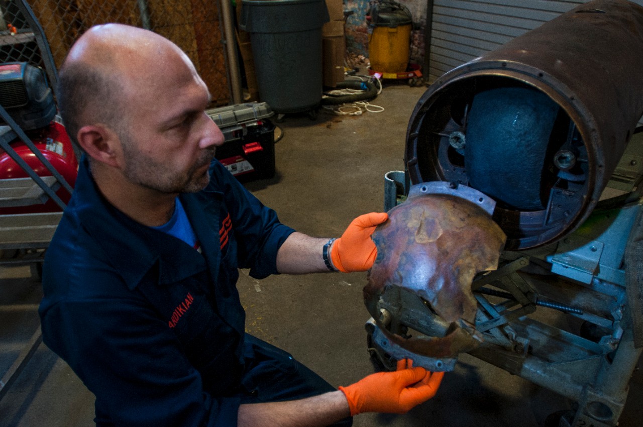 Conservator Paul Mardikian holds the oil shield in its original position over the fly wheel in the midsection of the torpedo. 