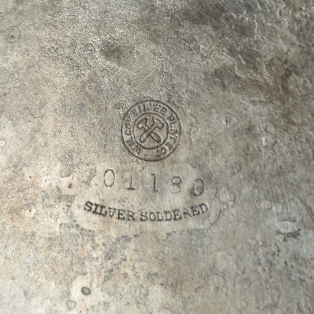 <p>Obverse Side: Hallmark on the reverse side with two crossing hammers within a circle and the words “Wilcox Silver Plate Co.” around the outside of the circle. Below the circle are the numbers “01188” and the words “Silver Soldered”.</p>