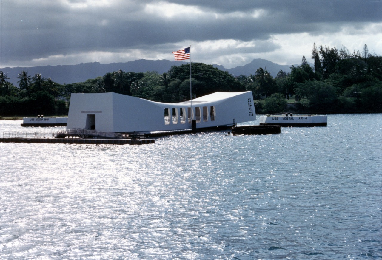 Color photo of the sun shining on the Arizona Memorial and the water surrounding it.