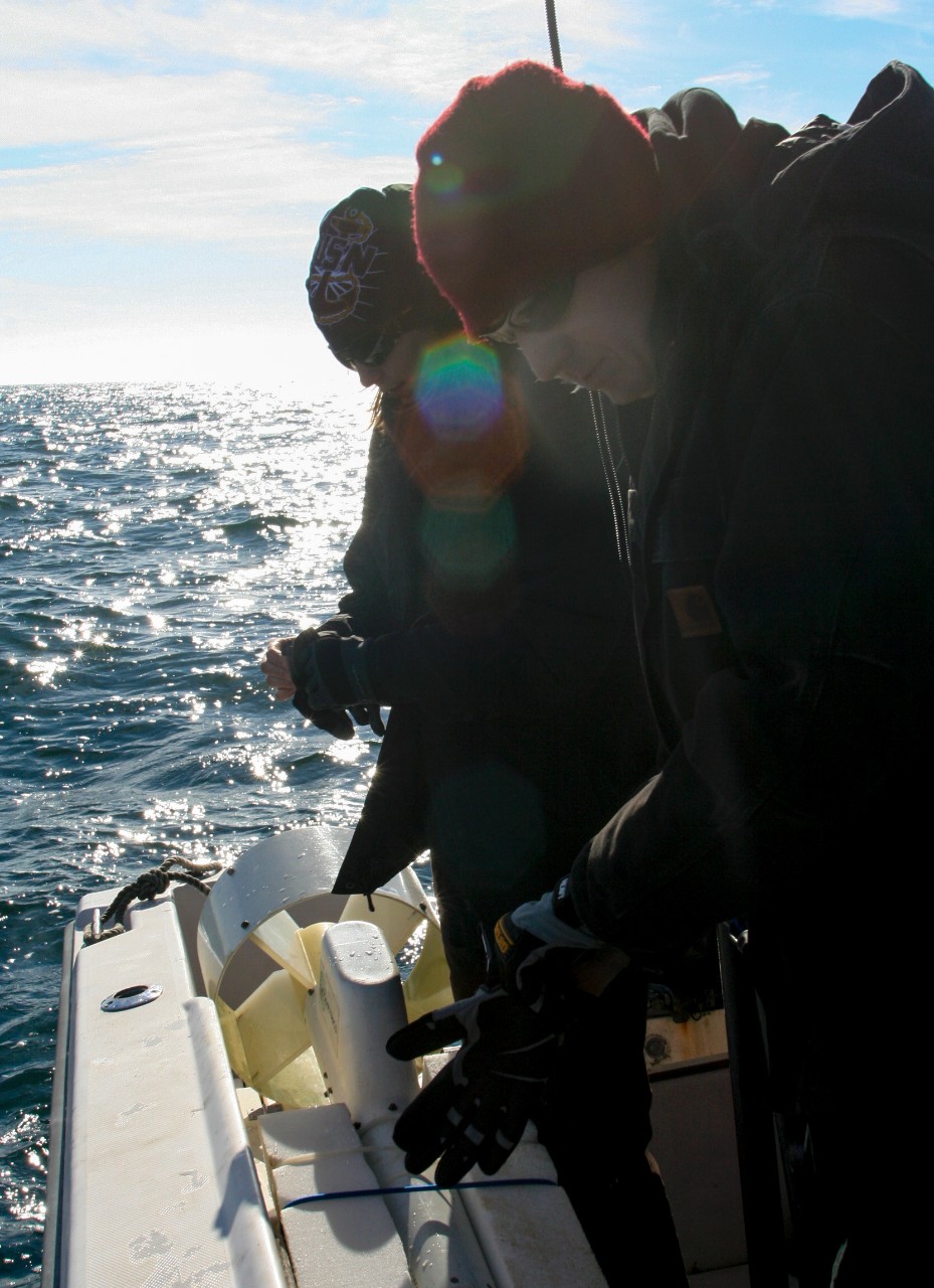 Two people with coats and hats on a boat getting equipment ready for a survey.