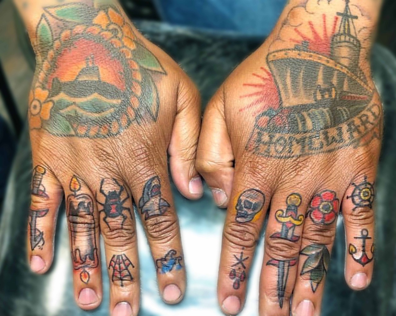 Hand tattoos of a submarine, battleship with the word "homeward," and individual finger tattoos of various nautical designs.