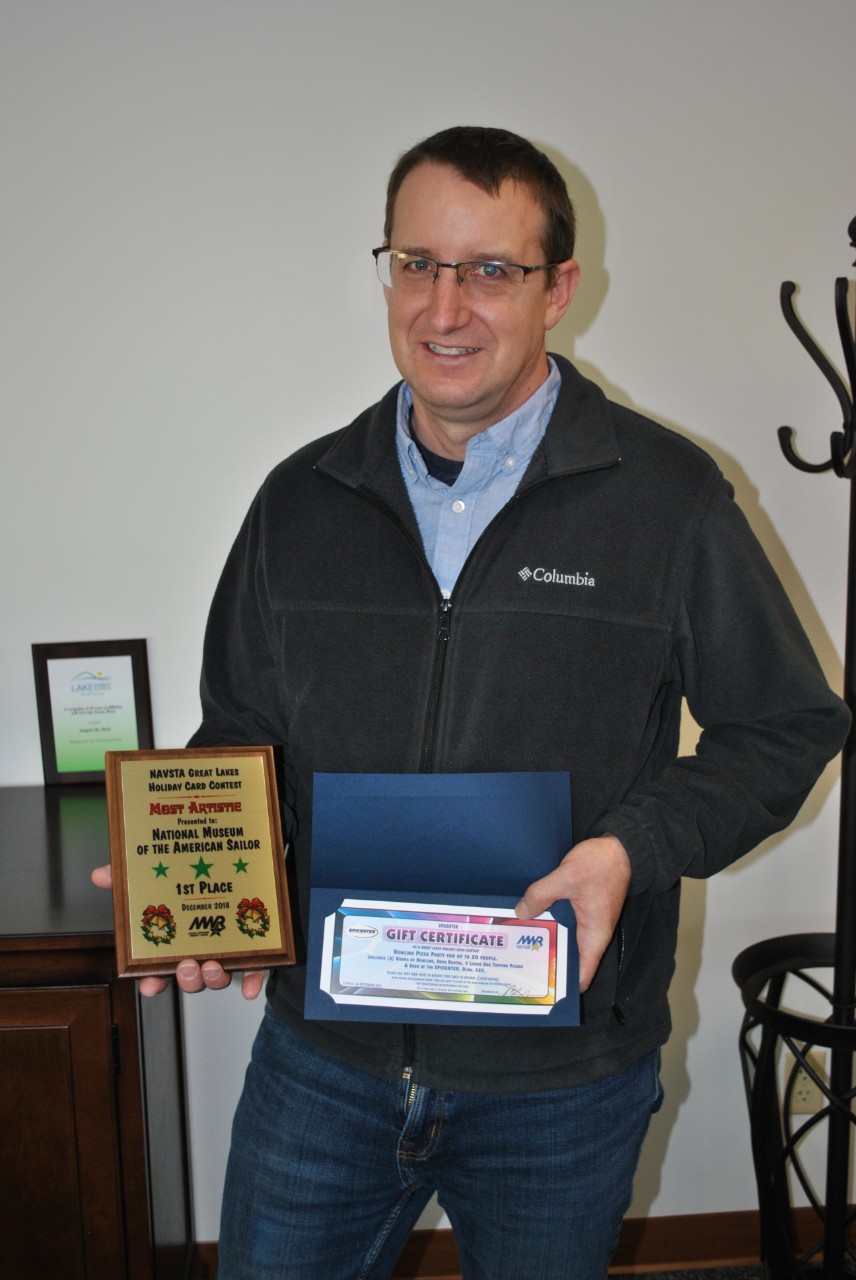 Ian LaBlance, NMAS Exhibit Specialist accepting the 1st Place Award in the “Most Artistic” category of the Naval Station Great Lakes Morale, Welfare and Recreation Department’s Annual Holiday Card Challenge.