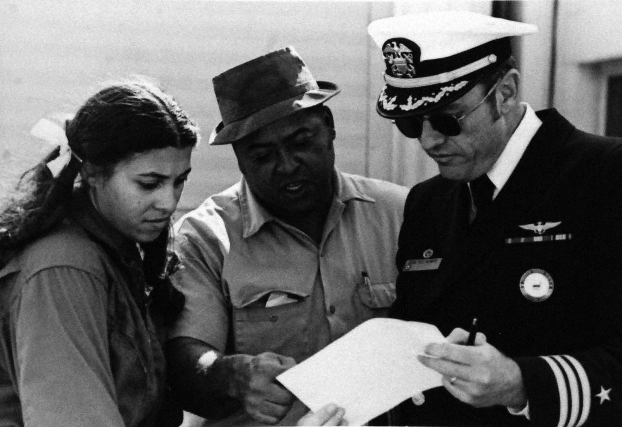 428-GX-USN-1160763: Navy Aviation Officer Candidate Jill Brown, 1974.  Her father, Mr. Gilbert Brown, and Commander Ted Hewitt look over some paper work prior to a training flight.  Hewitt is the Commanding Officer of Miss Brown’s unit.  She is the first African-American to qualify for training as a military pilot.  Photographed by PHC James E. Markham, received January 1975.  Official U.S. Navy Photograph, now in the collections of the National Archives.  
