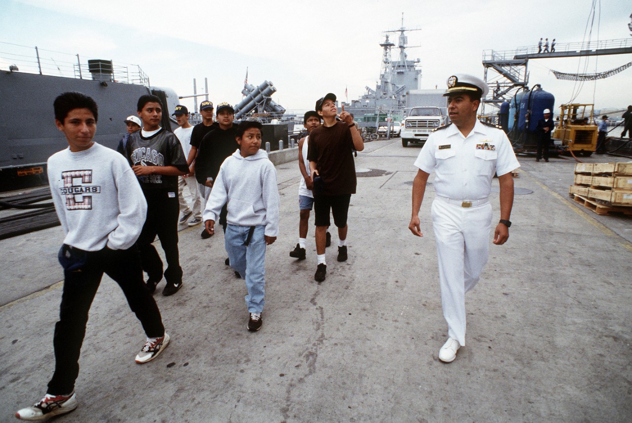 330-CFD-DN-ST-94-02147:   Lieutenant Rich Torez, 1993.  Torez, a member of the Association of Naval Services Officers (ANSO), escorts junior Reserve Officer Training Candidates (ROTC) Hispanic students from Orange Glen and Escondido High Schools down the pier at 32nd St. to USS Lake Champlain (CG-57) for a tour at San Diego, California.   USS Long Beach (CGN-9) is in the background.  Photographed October 1, 1993 by PH1 Charles W. Alley.    Official U.S. Navy photograph, now in the collections of the National Archives.  