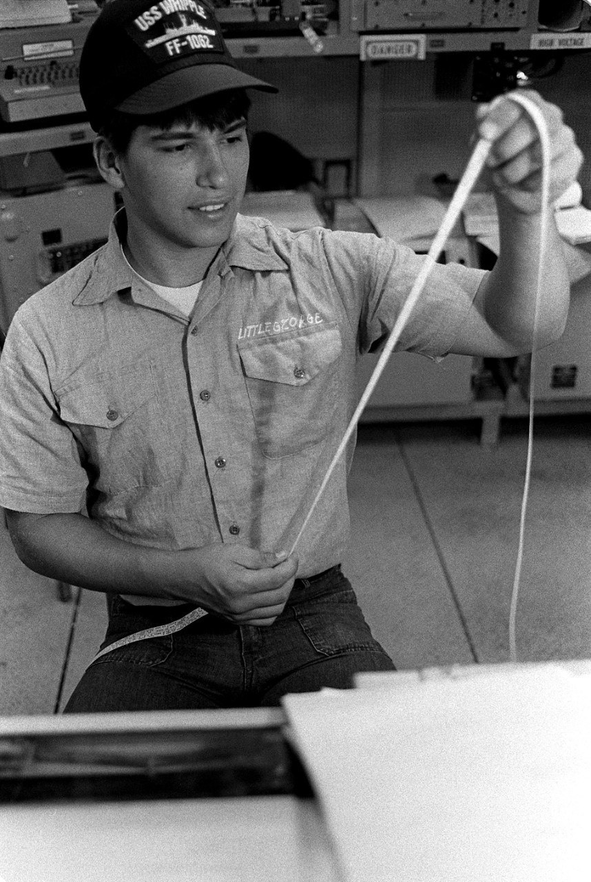 330-CFD-DN-SN-84-01402:   Seaman Roger Bruce Littlegeorge, 1983.   Littlegeorge was a radioman aboard the frigate USS Whipple (FF-1062), proofreads a perforated tape in the ship's communication center.  Littlejohn is an American Indian.  Official U.S. Navy photograph, now in the collections of the National Archives.  
