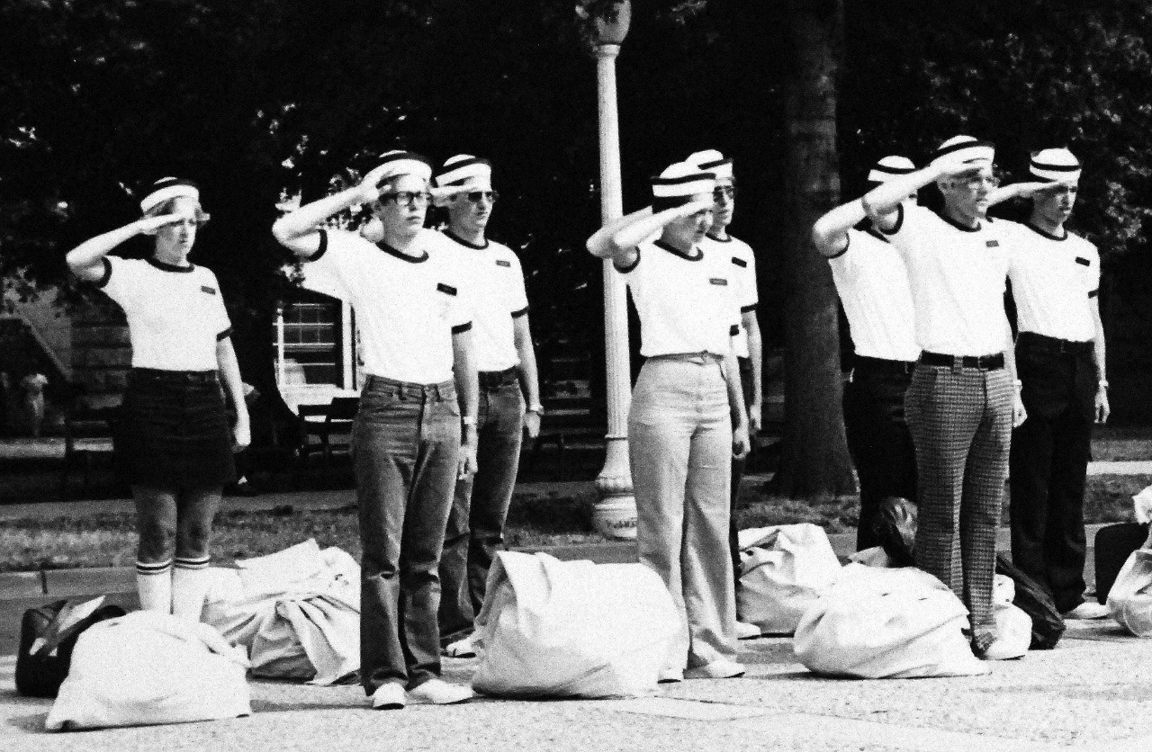 428-GX-USN-1168170:   New Midshipmen return a hand salute, July 1976.  The new class includes women for the first time at the Naval Academy, Annapolis, Maryland.  Marie L. Cote is on the left.  Photographed by JO2 Pete Sunberg, July 1976.   Official U.S. Navy Photograph, now in the collections of the National Archives. 