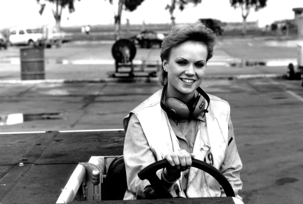 330-CFD-DN-ST-86-02117:    Female Plane Director, March 1984.   The director drives a tow tractor on the flight line at U.S. Naval Air Station, Sigonella, Sicily, Italy.  Photographed by PHC Chet King.  Official U.S. Navy photograph, now in the collections of the National Archives.  