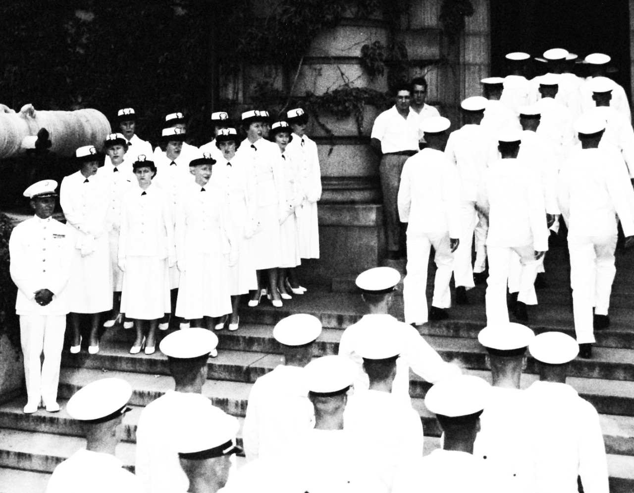 USN 708656:  WAVE guests at Annapolis, July 1952.  Thirteen WAVE officers of the group of eighty-five WAVES and ex-WAVES who visited the U.S. Naval Academy at Annapolis, Maryland, on July 27, 1952, receive the “march past” from a group of middies on the steps of Bancroft Hall.  Lieutenant Colonel Dale H. Heely, USMC, (left), of the faculty, was one of the escort officers to the visitors.  The group was guests of Vice Admiral Harry W. Hill, USN, Superintendent of the Academy, the faculty, and midshipmen students.  The visit was part of the celebration of the Tenth Anniversary of the WAVES inclusion as an official branch of the U.S. Navy.  Photograph released July 28, 1952.  Official U.S. Navy photograph, now in the collections of the National Archives.  