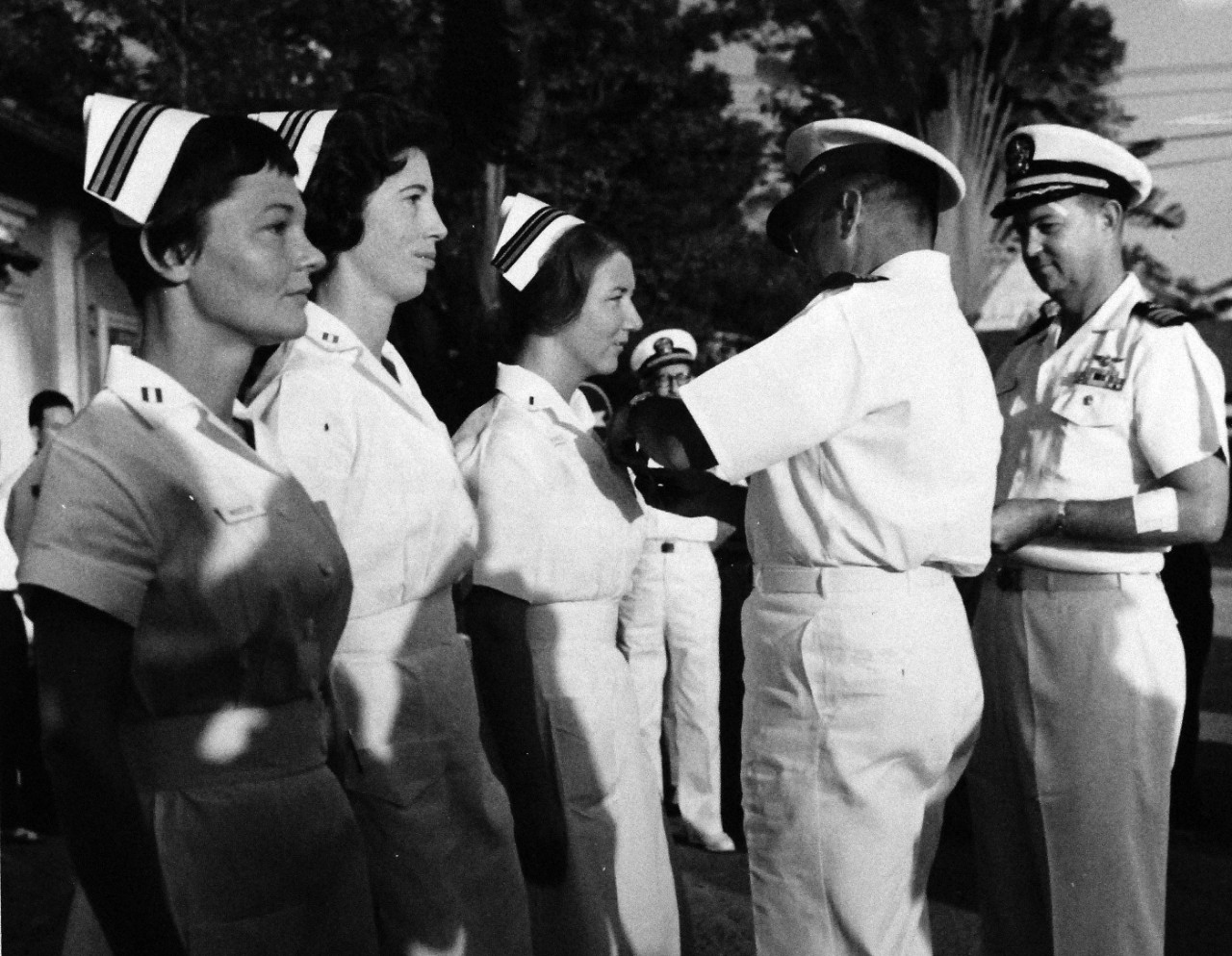 KN-10517:   Purple Hearts awarded to U.S. Navy Nurses, January 1965.   Three of the four U.S. Navy Nurses awarded the Purple Heart in Vietnam, receive their awards from Captain Archie Kuntze, Commanding Officer, U.S. Naval Support Activity, Saigon.  The nurses (left to right): Lieutenant Barbara J. Wooster; Lieutenant Ruth A. Mason; and Lieutenant Junior Grade D. Reynolds, are the first women to receive the medal in Vietnam.  Another nurse Lieutenant Francis L. Crumpton, was flown to Clark Air Base, Philippines, earlier for treatment.  The nurses, although injured in the Communist bombing of the HQ on Christmas Eve, refused medical treatment for themselves while rendering First Aid to others wounded by the explosion.  Commander Miles D. Turley, Executive Officer of the Naval Support Activity (right), assists his Commanding Officer in the presentation.  Turley was wounded New Year’s Day while investigating reports of sniper fire on water skiers in the Saigon River.  Photograph released January 15, 1965.  Official Department of Defense photograph, now in the collections of the National Archives.   (Black and White Only).  
