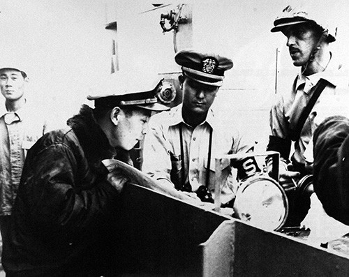 330-PS-9711 (428-GX-710560):  Officers of the Japanese Navy, U.S. Navy, and U.S. Marine Corps combine their efforts to aid Typhoon Vera victims near Nagoya, Japan.  Studying maps and charts of the Nagoya disaster area on board a Japanese landing craft are Lieutenant Junior Grade Chujyo Kodo, Japanese Maritme Self-Defense Force; Lieutenant Junior Grade Richard L. Takakashi, USN, attached to the USS Kearsarge (CVA 33) and Captain John E. Dorham, USMC, Commander of the Marine Detachment on board Kearsarge.  This LCM is being used to transport water, bread, and medicine into flooded areas, 7 October 1959.  Official U.S. Navy Photograph, now in the collections of the National Archives.     