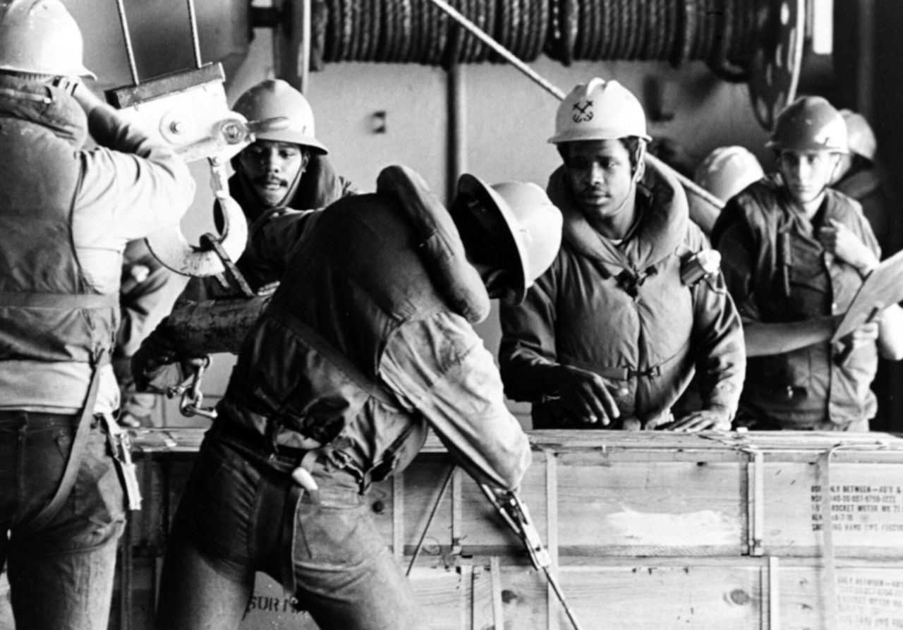 NH 97659:  USS Forrestal (CV-59).  Crewmen secure the cable and hook on a box, during underway replenishment operations in the Atlantic Ocean, 26 June 1976. Photographed by PH1 G. Burgess. Naval History and Heritage Command Photograph.   