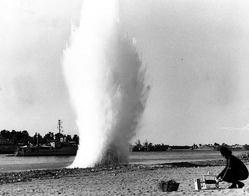 Ordnance discovered in shallow waters of canal is detonated by French Navy diver.  In the background is French Navy minesweeper serving as support ship.   Photographed by LCDR C.C. Bottinni, French Navy.   NHHC Photograph Collection, Navy Subject Files. 