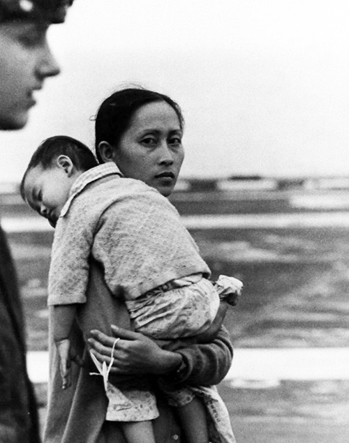 127-GVB-279-A150894:   Operation Frequent Wind.  Evacuation of Phnom Penh and Saigon, April 29, 1975.  Shown:   A Vietnamese woman, carrying her son, is given a numbered tag as she arrives onboard USS Hancock (CV-19).  Her belongings will be tagged with the same number due to the language barrier between the refugees and Marines.   Official U.S. Marine Corps photograph, now in the collections of the National Archives.   