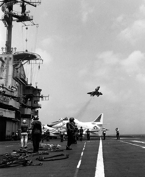 NH 97497:  USS Lexington (CVT/AVT-16), flight deck activity during the 1970s or 1980s).  A TA-4J Skyhawk is parked in the center as another passes overhead.   NHHC Photograph Collection.