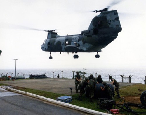 Civilians fleeing Liberia's civil war watch as Marine Medium Helicopter Squadron 162 (HMM-162) CH-46E Sea Knight helicopter lands at the U.S. Embassy during Operation Sharp Edge.   The helicopter will carry a group of evacuees to one of the ships of an amphibious ready group on station off the Liberian coast.   The ready group is also providing personnel and logistic support for the embassy, 27 August 1990.   Photographer: JO2 William G. Davis III.   NHHC Photograph Collection, Navy Subject File. 