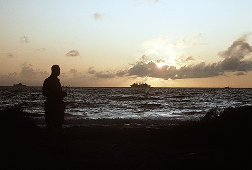 330-CFD-DN-ST-93-02849: Operation Restore Hope. The rising sun silhouettes a U.S. serviceman looking out at ships off the coast during the multinational effort. Photographed by JO1 Joe Gawlowicz, December 1992. Official U.S. Navy photograph, now ...