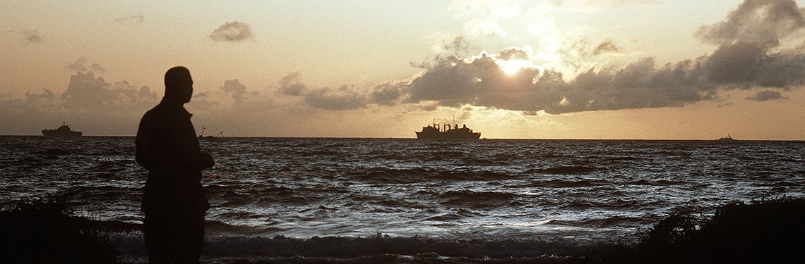 330-CFD-DN-ST-93-02849: Operation Restore Hope. The rising sun silhouettes a U.S. serviceman looking out at ships off the coast during the multinational effort. Photographed by JO1 Joe Gawlowicz, December 1992. Official U.S. Navy photograph, now ...
