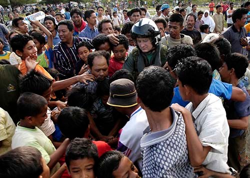 050106-N-4166B-207: Residents of Meulaboh, Sumatra, Indonesia, gather around Aviation Warfare Systems Operator 2nd Maxwell Bjerke as he hands out water that was delivered by his HH-60H Seahawk helicopter. Photographed on January 6, 2005 by Photog...
