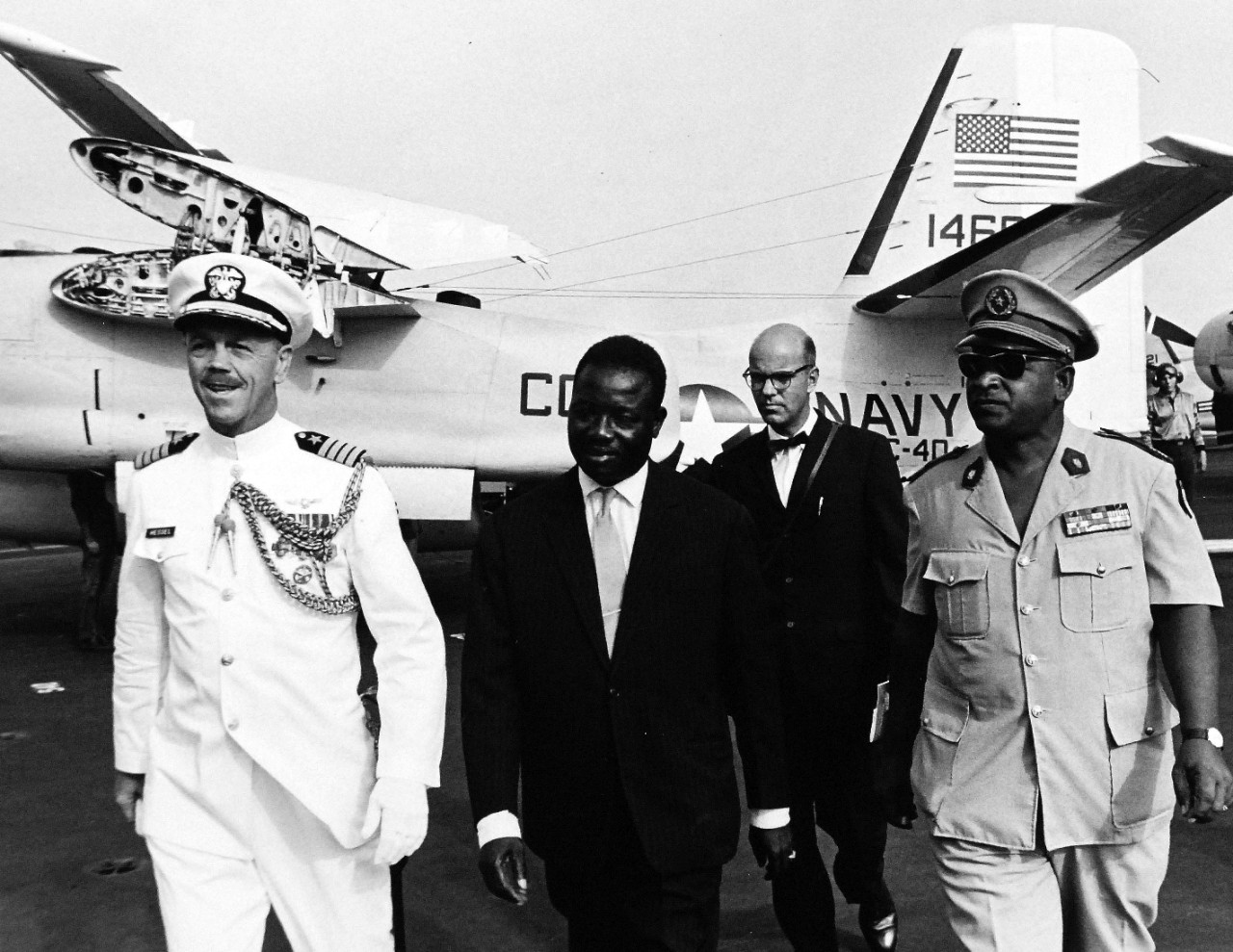 330-PSA-178-64 (USN 11042204):  Operation Sea Orbit, 1964.   Officials at Dakar, Senegal, were flown to USS Enterprise for an air demonstration as the nuclear task force sailed down the coast of Africa in the first phase of the global cruise.  Captain E.W. Hassel, Chief of Staff for the Commander of the Task Force escorts Senegalese cabinet officials.   Master caption:  Operation Sea Orbit has completed the first three weeks of its round-the-world cruise proving conclusively the feasibility of operation nuclear surface ships over great distances on a self-sustaining basis.  Sea Orbit is the first world cruise of the surface nuclear ships.  The task force is made-up of USS Enterprise (CVN-65), USS Long Beach (CLGN-9), and USS Bainbridge (DLGN-25).   The world cruise has a dual mission.  It offers practical experience in operation of nuclear-powered warships independent of support ships, a fast impractical for conventionally powers ships.  Equally important, and immediately evident is the opportunity to win friends in areas not frequently visited by U.S. Navy ships, and to show the world an all nuclear element of the world’s greats power for peace.  Two other world circumnavigations were made by U.S. nuclear vessels, both submarines.  Photograph released August 22, 1964.  Official U.S. Navy Photograph, now in the collections of the National Archives.   (2015/11/03).