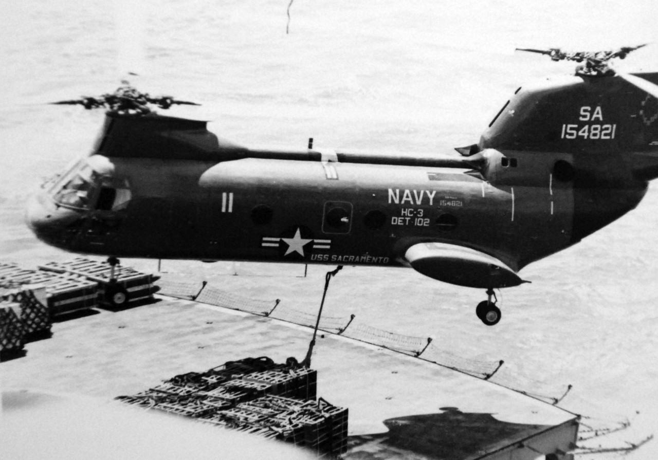 428-GX-USN-1149950:  USS Enterprise (CVAN-65), 1971.  A CH-46A “Sea Knight” aerial replenishment helicopter of Helicopter Combat Support Squadron Three (HC-3), Detachment, prepares to transfer a pallet of bombs from the deck of the Fast Combat Support Ship USS Sacramento (AOE-1) to the carrier.    Photographed by Lieutenant Junior Grade White, August 1971.  Official U.S. Navy Photograph, now in the collections of the National Archives.  (2017/11/29).  