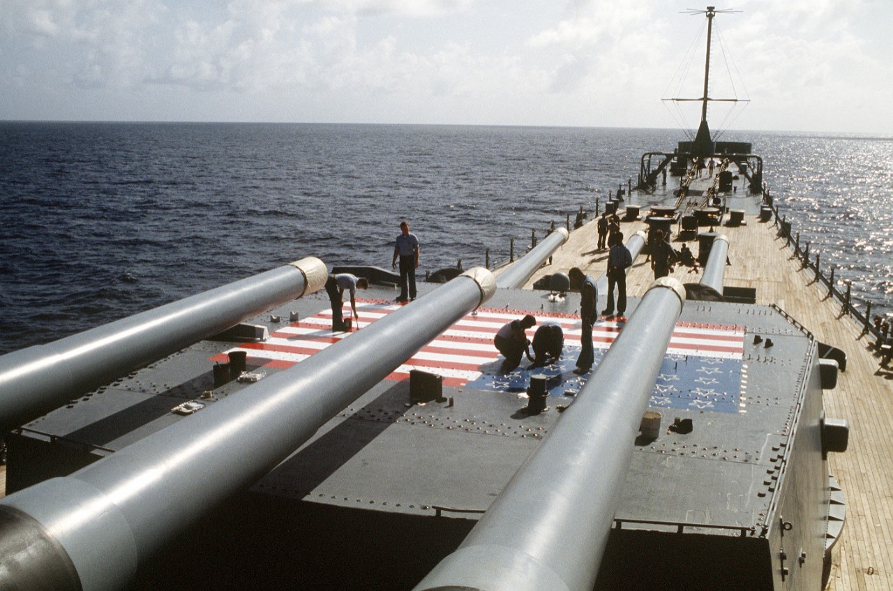 330-CFD-DN-ST-85-07818:  USS Iowa (BB-61), 1984.    The US flag is painted on top of the No. 1 16-inch gun turret aboard the battleship USS Iowa (BB 61), 6/15/1984.  PH1 (SW) Jeff Hilton, USN.  (OPA-NARA II-2016/01/07).