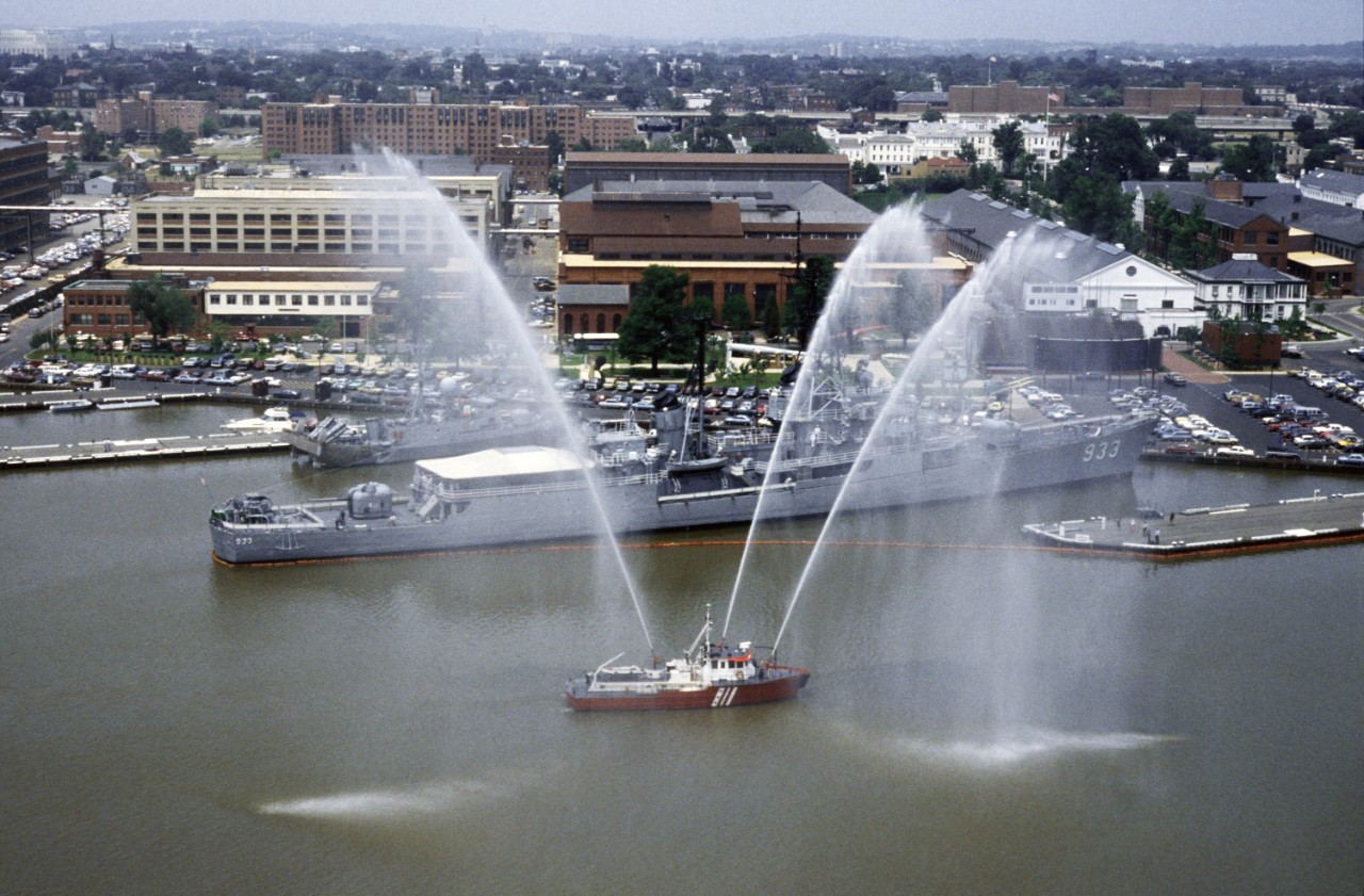 330-CFD-DN-ST-86-07371:  Washington Navy Yard, circa 1986.   The District of Columbia fire boat John H. Glenn, Jr. shoots streams of water skyward to welcome the US Coast Guard (USCG) training bark USCG Eagle (WIX-327), not visible in view, to the Washington Navy Yard.  Moored at Pier No. 3 is the memorial destroyer USS Barry (DD-933) and moored at Pier 2 is the missile hydrofoil patrol boat USS Taurus (PHM-3). Official U.S. Navy Photograph, now in the collections of the National Archives.      