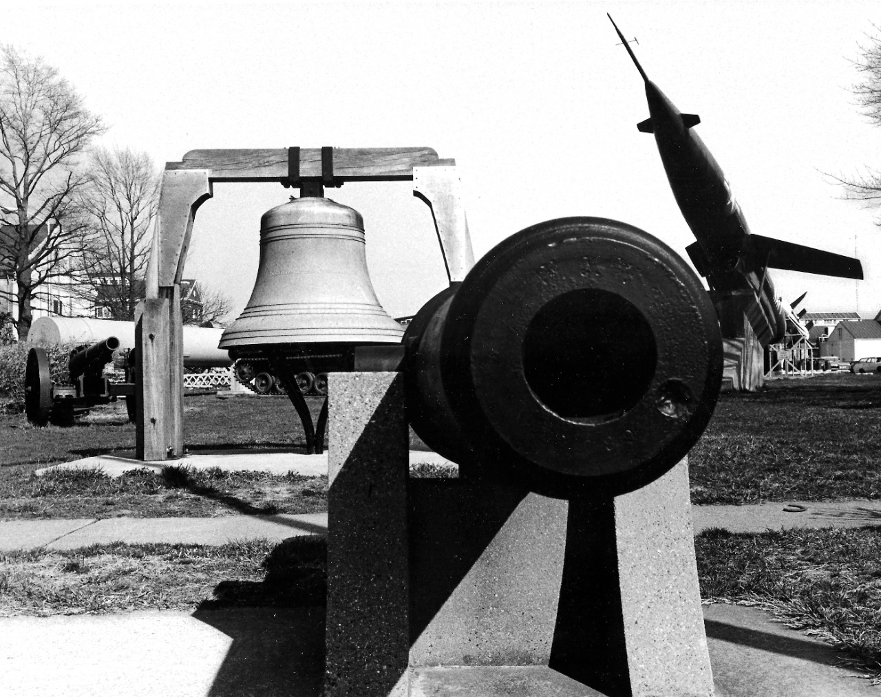 NMUSN-146:  Willard Park, Washington Navy Yard, Washington, D.C. 1970s.   View faces north, showing a smooth-bore cannon barrel, with a lighthouse bell from 1897 behind.   A Regulus II missile is to the right.   National Museum of the U.S. Navy Photograph Collection.  