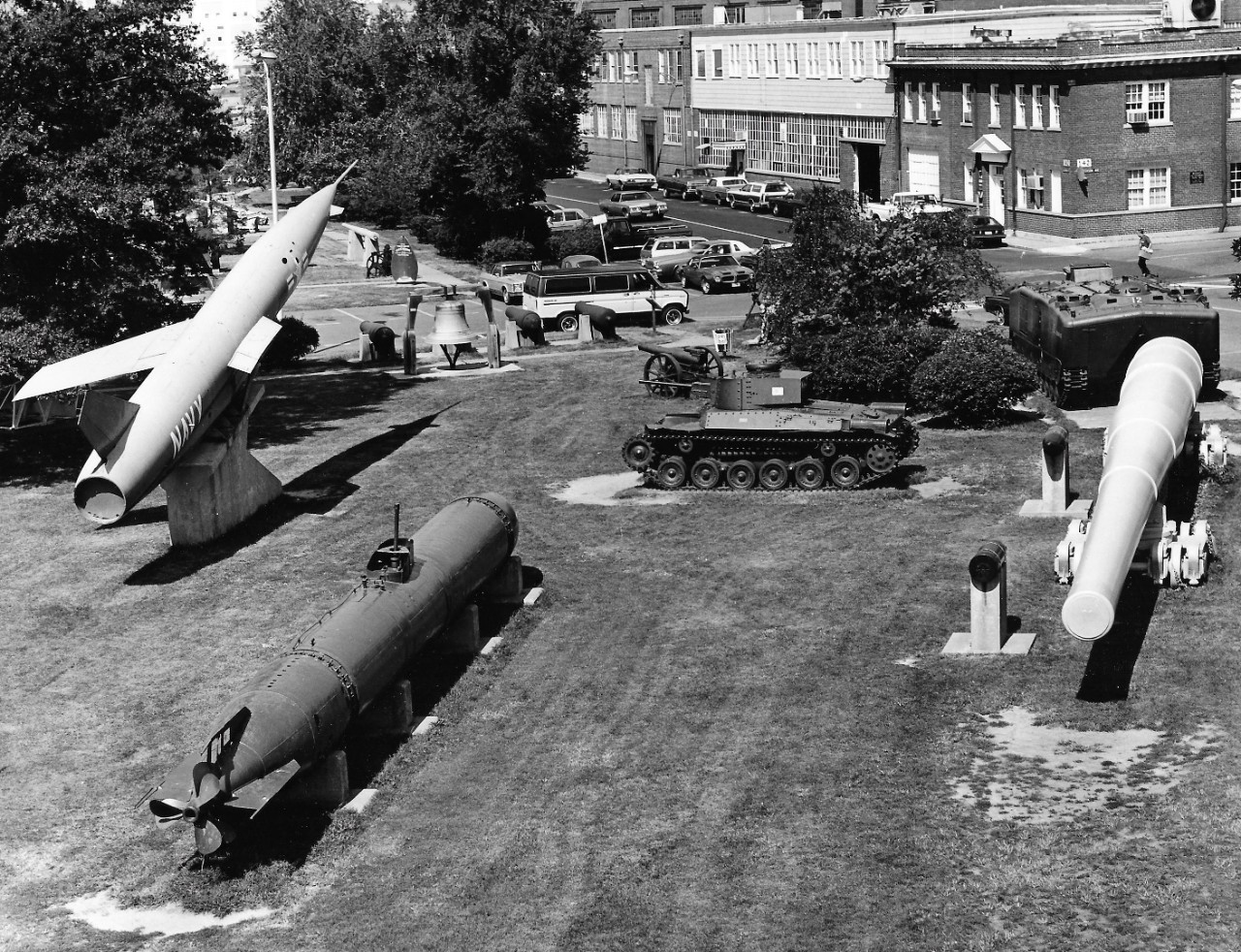 NMUSN-153:  Willard Park, Washington Navy Yard, Washington, D.C. 1970s.    View looks west.    Right to left.   Regulus II missile; Lighthouse Bell, 1897; Japanese Tank; 16” Gun; Japanese two-man submarine.   National Museum of the U.S. Navy Photograph Collection.   