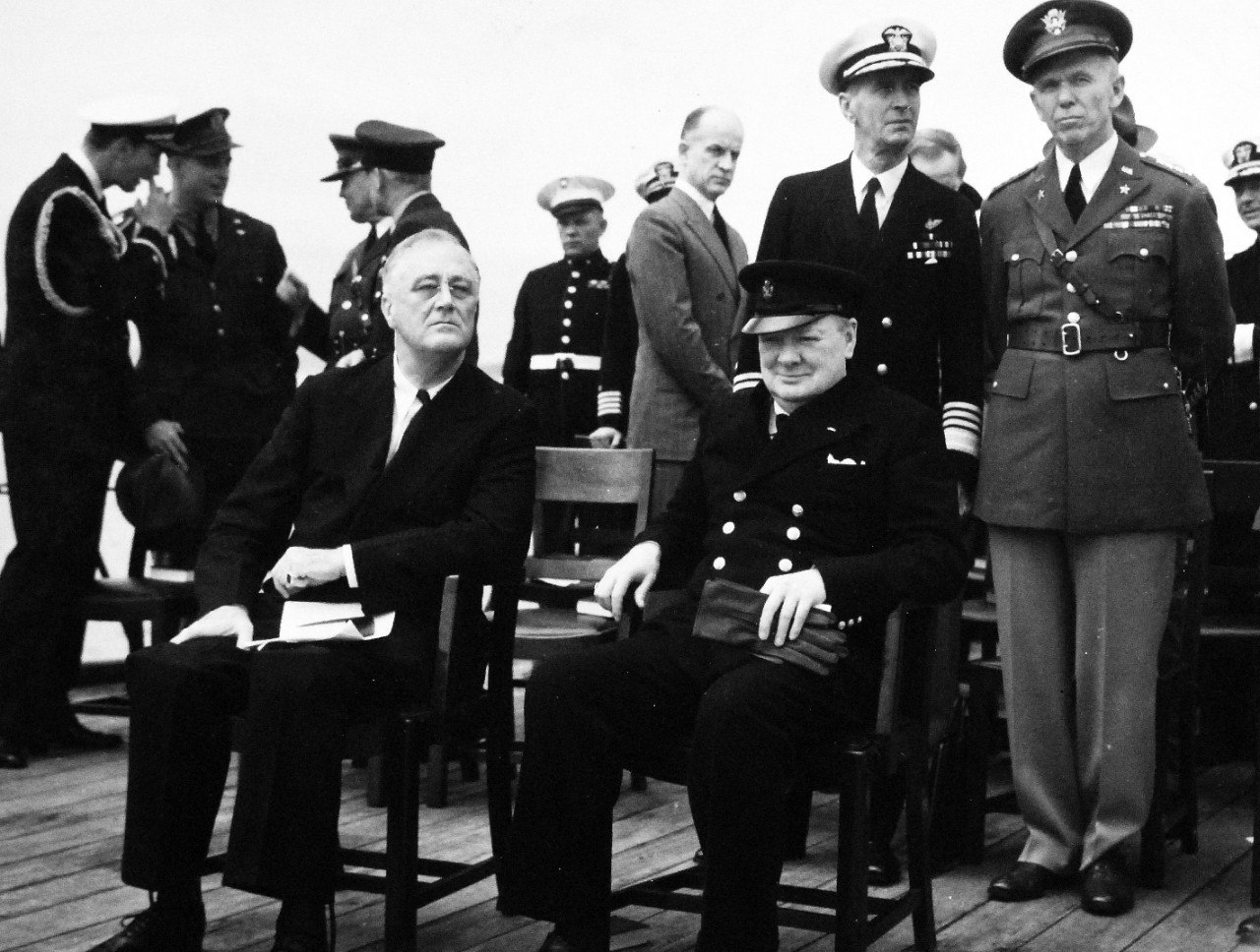 80-G-26870: Atlantic Charter, August 1941.  Informal group photograph including President Franklin D. Roosevelt and Prime Minister Winston S. Churchill on deck of HMS Prince of Wales following church services during the Atlantic Charter.  Shown behind Roosevelt and Churchill are Admiral Ernest J. King and General George C. Marshall.   Photograph released August 1941.   Official U.S. Navy Photograph, now in the collections of the National Archives.  (2016/03/22).