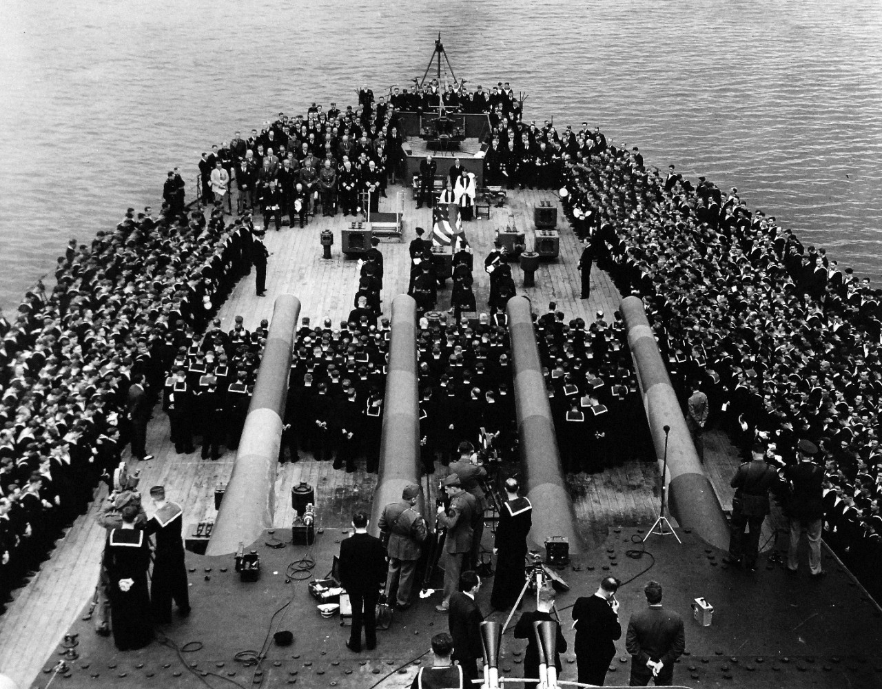 80-G-26878: Atlantic Charter, August 1941.  Informal group photograph including President Franklin D. Roosevelt and Prime Minister Winston S. Churchill on deck of HMS Prince of Wales during church services during the Atlantic Charter.  Upper left, President Roosevelt and Prime Minister Churchill are seated in front of their respective standing staff members.  Big guns of the British battleship range over the gathering.  Photograph released August 1941.   Official U.S. Navy Photograph, now in the collections of the National Archives.  (2016/03/22).
