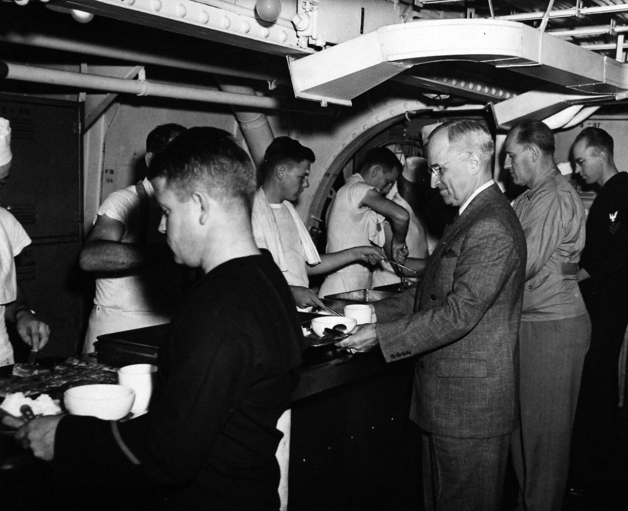 80-G-49928:  Potsdam Conference, July-August 1945.  President Harry S. Truman onboard USS Augusta (CA-31) en-route to Antwerp for the “Big Three” Conference.  Shown:  Being served in crew’s mess hall.  Faces which can be seen in the picture are:  (left to right):  S1/C Albert Rice; S1/c J.W. Leinback; S1/C .W. Smith, the President, a secret service man and PhM2/C Elmo C. Buck.  Photograph received July 18, 1945.  Official U.S. Navy Photograph, now in the collections of the National Archives.  (2016/02/23).