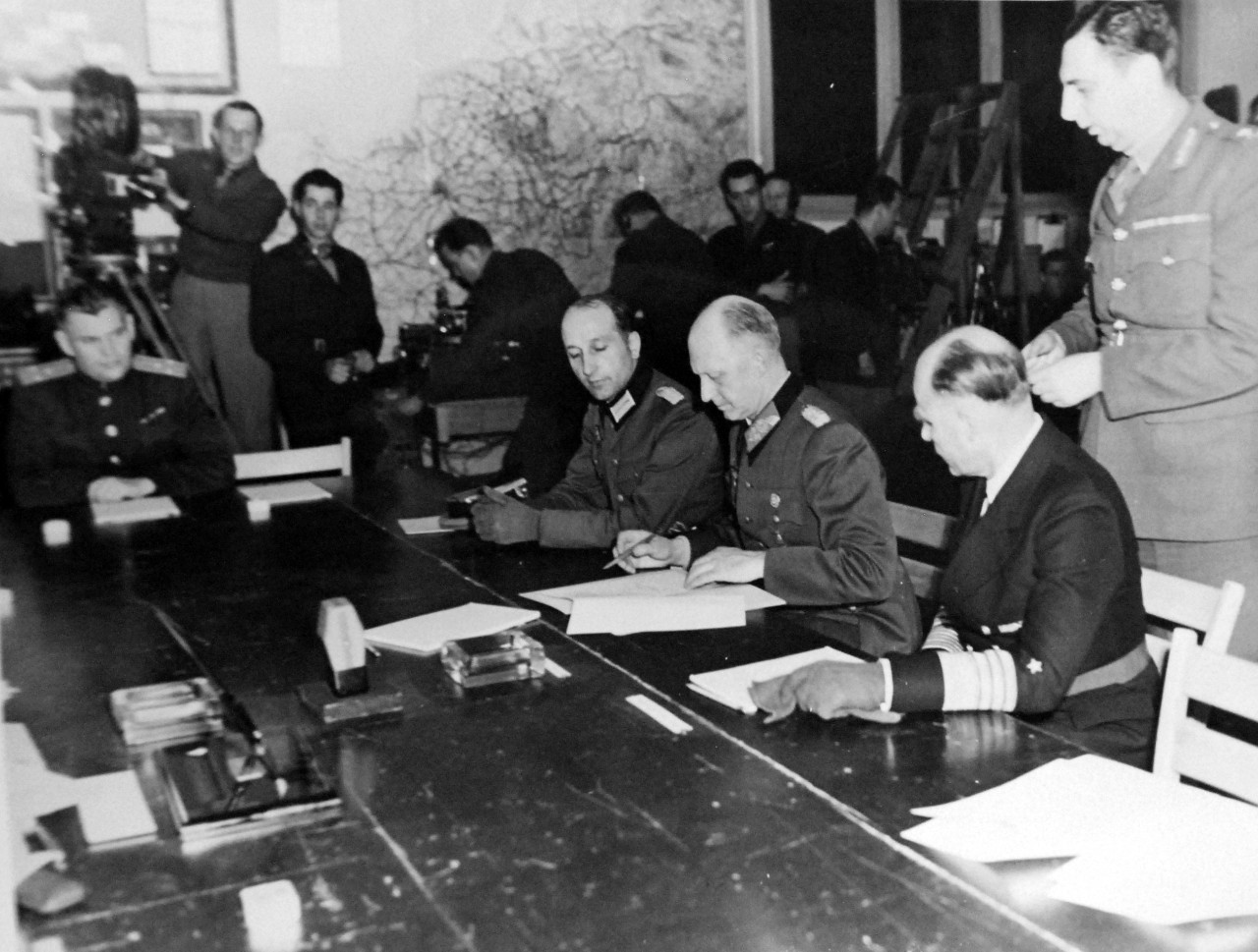 111-SC-27261: Surrender of Germany, 7 May 1945. Colonel General Alfred Jodl, German Chief of Staff, under the Doenitz Regime, is here shown signing the document of “Unconditional Surrender” under which all remaining forces of the German army are bound to lay down their arms in unconditional surrender.  The scene is the War Room of Supreme Headquarters, Allied Expeditionary Forces, Reims, France.  On General Jodl’s left is General Admiral Von Friedeburg, of the Germany Navay, and on his right is Major Wilhelm Oxenius, of the German General Staff.  Standing behind General Admiral Von Friedenburg is Major General K.W.D. Strong, G-2, SHAEF. U.S. Army Photograph.  Courtesy of the Library of Congress Collection, Lot-8988. (2015/10/16).