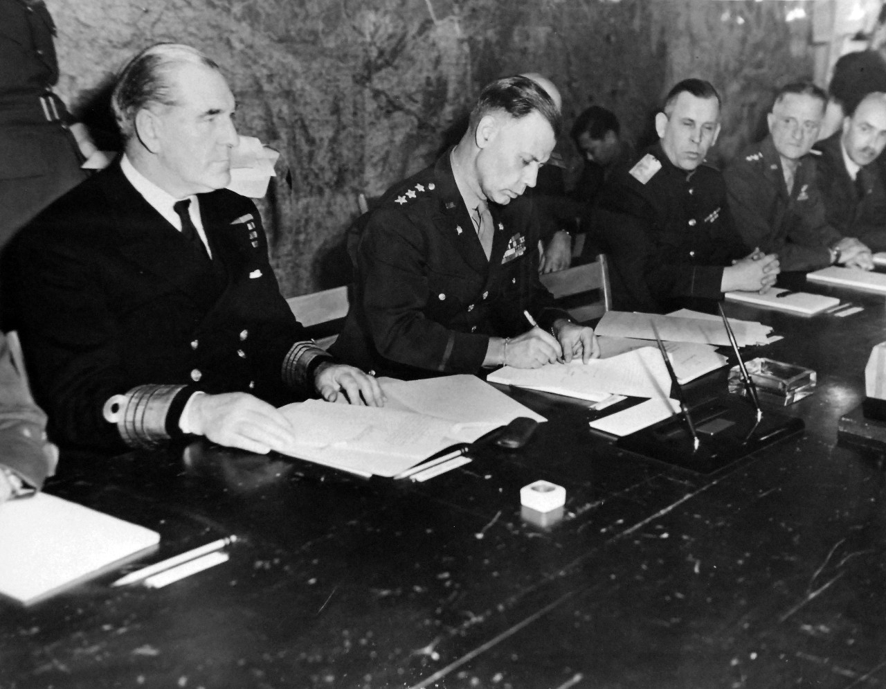 111-SC-27262: Lieutenant General W.B. Smith, Chief of Staff, SHAEF, affixes his signature to the Unconditional Surrender document on behalf of the Allied High Command after it had been signed by the representatives of the German government sitting across the table from him at SHAEF, Reims, France.  On General Smith’s right is Admiral Harold M. Burrough, Commander in Chief, Allied Naval Expeditionary Forces.  On General Smith’s left is Major General Ivan Alexeyevich Susloparov of the Russian Artillery and General Carl A. Spaatz, CG, US Staff.  U.S. Army Photograph.  Courtesy of the Library of Congress Collection, Lot-8988. (2015/10/16).