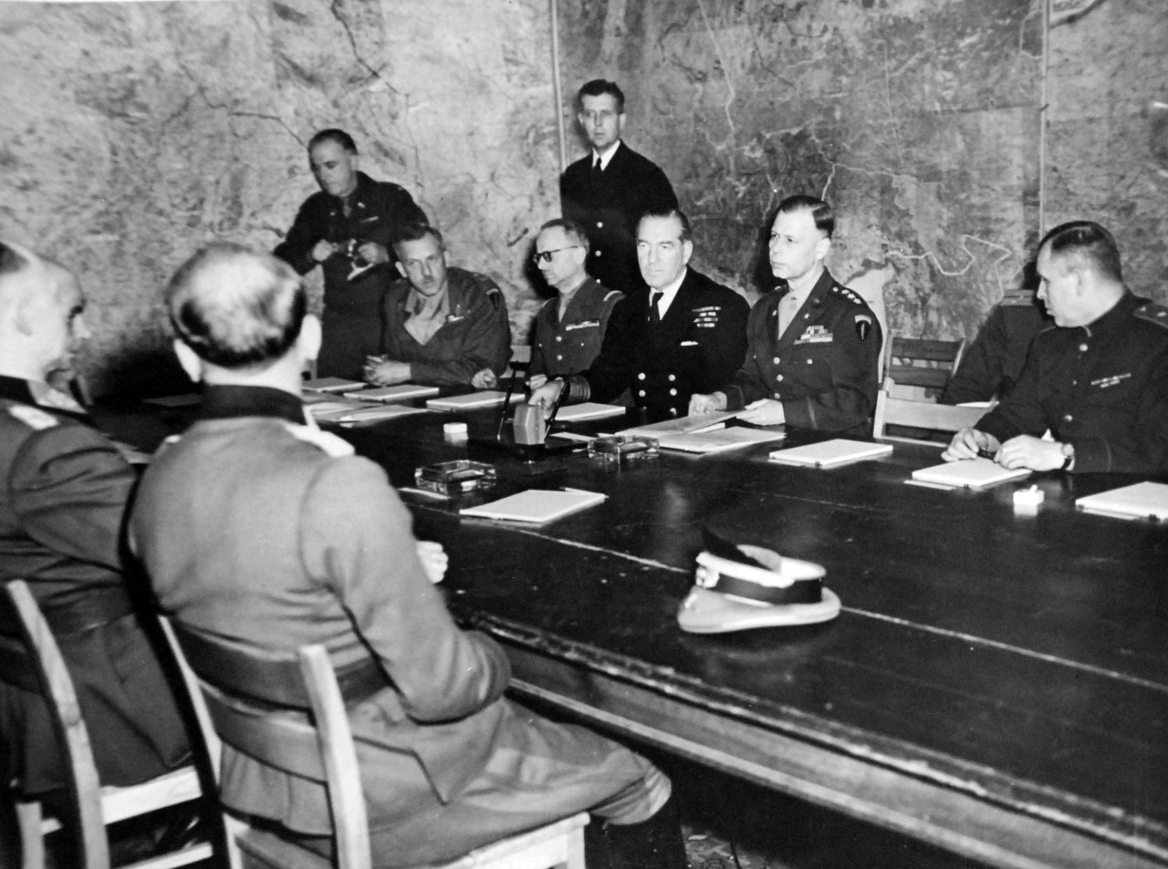 111-SC-27266: Surrender of Germany, 7 May 1945. Terms of Unconditional Surrender are here being dictated to the Representatives of the German government in the War Room of Supreme Headquarters, Allied Expeditionary Forces (SHAEF), at Reims, France.  In the picture, backs to camera, are Major Wilhelm Oxenius, of the German General Staff; (nearest camera) Colonel General Gustaf Jodl, German Chief of Staff; General Admiral Von Friedburg, of the German Navy, facing the camera on the far side of the table, seated are (left to right) Lieutenant General Sir F. E. Morgan, Deputy Chief of Staff; General Francois Sevez, Representative of General Alphonse Juin, French Chief of Staff; Admiral Harold M. Burrough, Commander in Chief, Allied Naval Expeditionary Forces; Lieutenant General W.B. Smith, Chief of Staff, SHAEF; and Major General of Artillery Ivan Alexeyevich Susloparov, Russian Representative.  Standing behind General Sevez is Captain H.C. Butcher, Naval Aide to General Eisenhower.  U.S. Army Photograph. Courtesy of the Library of Congress Collection, Lot-8988. (2015/10/16).