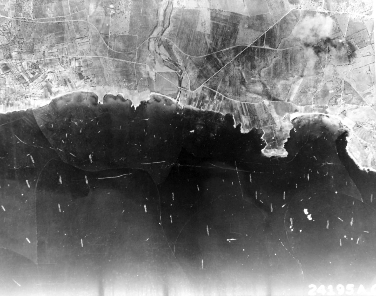 PR-13-CN-1971-246-10:  Operation Husky, July-August 1943.   U.S. Army Air Force Reconnaissance plane photograph shows part of the southeastern Sicilian coast, the day the Allies invaded.   Scores of our boats can be seen mostly transports and landing craft.  The smaller craft darting speedily among the large ships (indicated by their white wakes), are probably PT boats and unloading craft.  In bay on the right, LCT boats for unloading tanks are discernible at the beach.  Explosions in the water may be seen nearby.  Note airplane near this beach, and another at the mouth of the bay.  Shellbursts from land batteries can also be seen near the transports lying offshore.  U.S. Army Photograph:  24195A.  Courtesy of the Library of Congress.  (2017/05/26).  