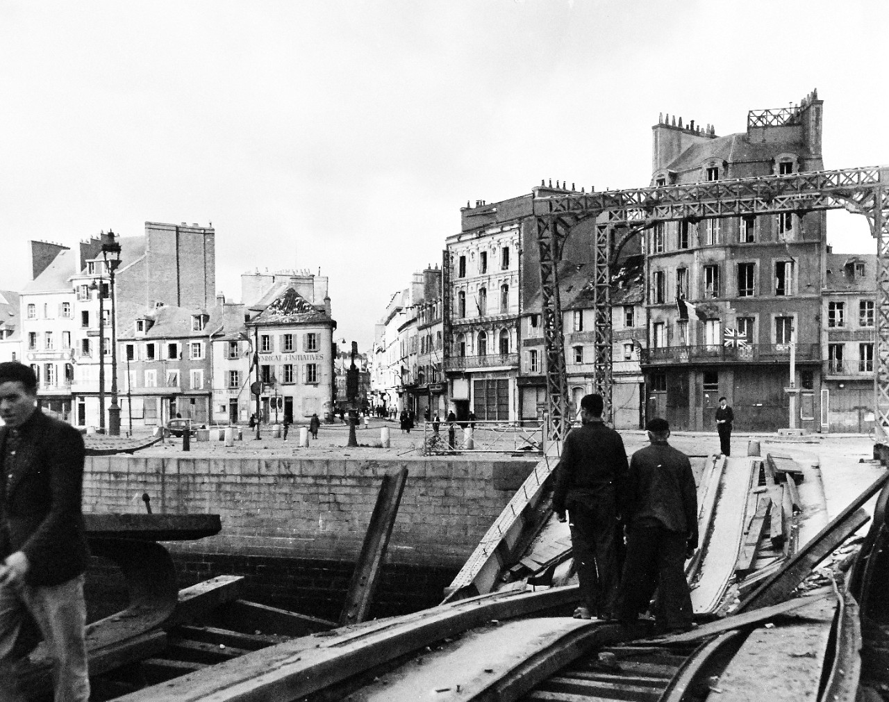 80-G-255916:  Normandy Invasion, Cherbourg, France, July 1944.    French civilians pass over damaged bridge to return to their homes in Cherbourg, France, after its liberation by Allies. Note the French and British flags flying from building at the right.   Photograph received October 28, 1944.   Official U.S. Navy Photograph, now in the collections of the National Archives.   (2014/11/05). 