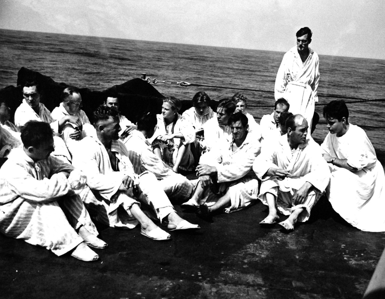 26-G-2587:  Normandy Invasion, German Prisoners, June 1944.  German Prisoners aboard a Coast Guard Manned Transport.  Aboard a Coast Guard-manned transport carrying them to the United States, these wounded and ailing German prisoners follow doctor’s orders and get plenty of fresh air and sunshine.  Attired in robes and slippers provided for them, they lounge on the open deck.  A Coast Guardsman chats at right with a prisoner who speaks English, June 1944.  Official U.S. Coast Guard Photograph, now in the collections of the National Archives.   (2015/5/19).  