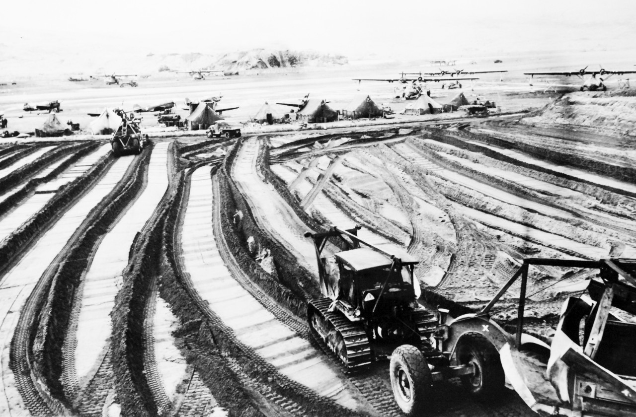 PR-13-CN-1991-34-6:    U.S. Naval Air Station, Adak, Alaska, 1943.      Tractors and grading machines grind out pathways in the stubborn soil of Adak, during the construction of bases on Aleutian strongpoints.  For many of the Seabees, the war has been a long struggle with stubborn tundra, an Herculean day-by-day routine of doing skilled work in bitter temperatures as they constructed the springboard for the final ouster of the Japanese from the Aleutians in 1943. Note the PBY aircraft in the background.    U.S. Navy Photograph.   Courtesy of the Library of Congress.  (2017/05/26).  Original photograph is curved.   