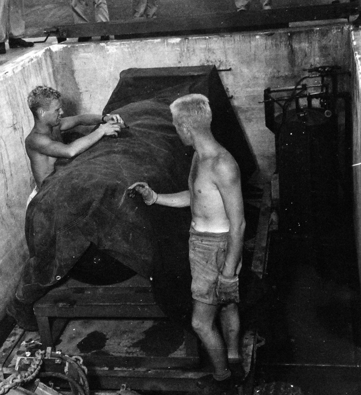 77-BT-121:  Tinian Island, August 1945.   Two enlisted men removing canvas cover from atomic bomb, Little Boy, in loading pit.   Official photograph of the Office of Chief of Engineers, now in the collection of the National Achives.   (2015/08/25). 