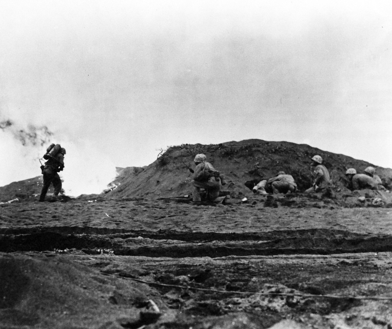 80-G-304845:  Battle for Iwo Jima, February 19, 1945.   A wave of Fourth Division Marines beginning an attack from the beach at Iwo Jima.   A die-hard Japanese soldier gets a blast of liquid flame.  Fifth Marine Division rifleman surround the dug-out ready to pour covering fire into the opening.  The flame thrower, supported by covering rifle fire, has been a basic weapon in the cave to cave-battle on the volcanic rock.  Photograph released February 19, 1945.  U.S. Navy Photograph now in the collections of the National Archives.  (2016/01/19).