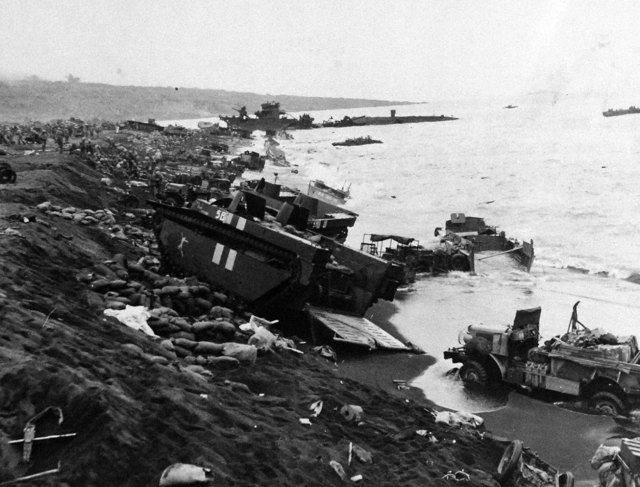 80-G-304851:  Battle for Iwo Jima, February 19, 1945.   Stalled and wrecked vehicles of Marines bagged down in soft Volcanic ash on beach of Iwo Jima were targets for Japanese mortermen who fired down from mountain over-looking beach D-Day.  First Aid stations (background) were set up among the debris.  Official U.S. Navy Photograph now in the collections of the National Archives.  (2016/01/19).