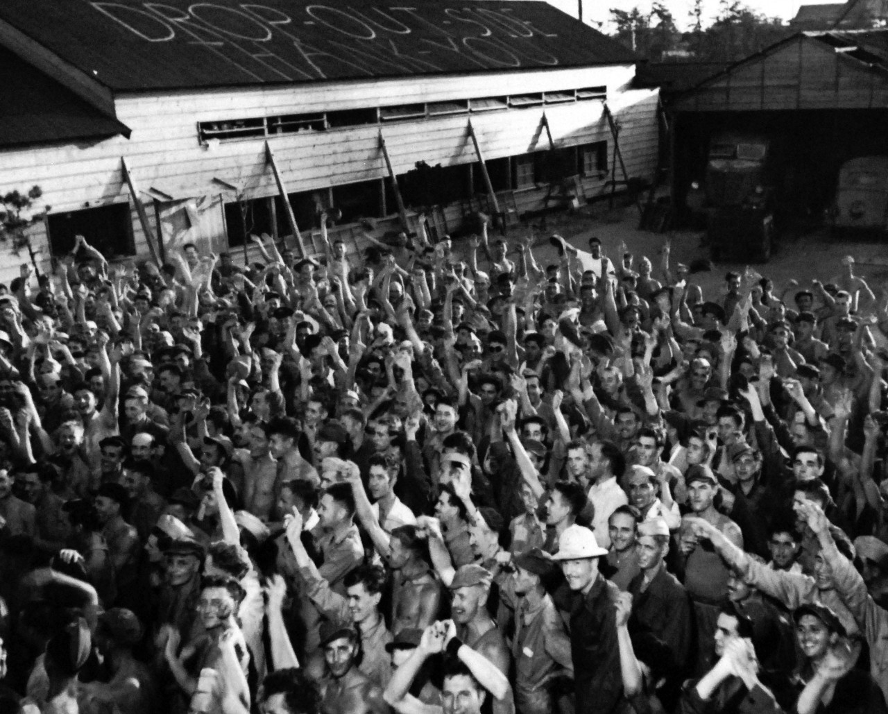 80-G-490467:   Allied Prisoner of War Camp, Omori, Japan, 1945.   Gaunt Allied Prisoners of War at Omori Camp, near Yokohama cheer rescuers from U.S. Navy.  Note the roof that reads, “Drop Outside.  Thank You.”   Photograph released August 29, 1945.  Official U.S. Navy photograph, now in the collections of the National Archives.  (2014/05/29).    The original is a small photograph.   