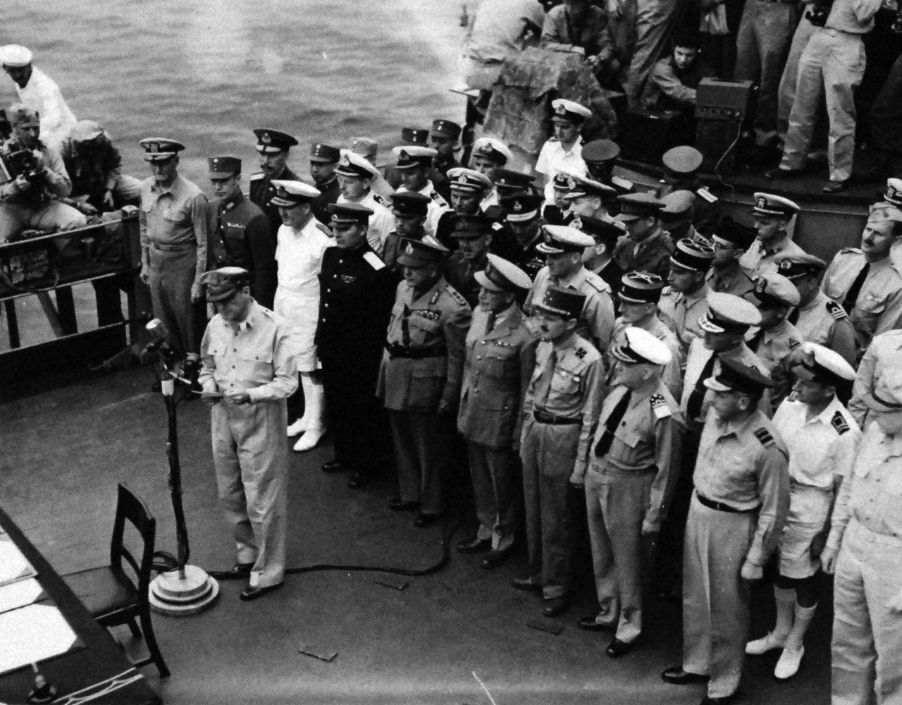 80-G-332694:  Formal Surrender of Japan, Tokyo Bay, September 2, 1945.  General of the Army Douglas MacArthur, Supreme Allied Commander, reading his speech to open the surrender ceremonies, on board USS Missouri (BB-63).  The representatives of the Allied Powers are behind him, including (from left to right): The U.S. representative, Fleet Admiral Chester W. Nimitz, USN;Representative of China, General Hsu Yung-chang; Admiral Sir Bruce Fraser, RN, United Kingdom; Lieutenant General Kuzma Derevyanko, Soviet Union; General Sir Thomas Blamey, Australia; Colonel Lawrence Moore Cosgrave, Canada; General Jacques LeClerc, France; Admiral Conrad E.L. Helfrich, The Netherlands and Air Vice Marshall Leonard M. Isitt, New Zealand.  This view is usually shown from the other side.   One can possibly see the photographers of those famous images. Photographed by Lieutenant C.A. Poots. Photographed from atop Missouri's 16-inch gun turret # 2.    Official U.S. Navy photograph, now in the collections of the National Archives.    (2015/11/17). Note, the original is a very small photograph.   