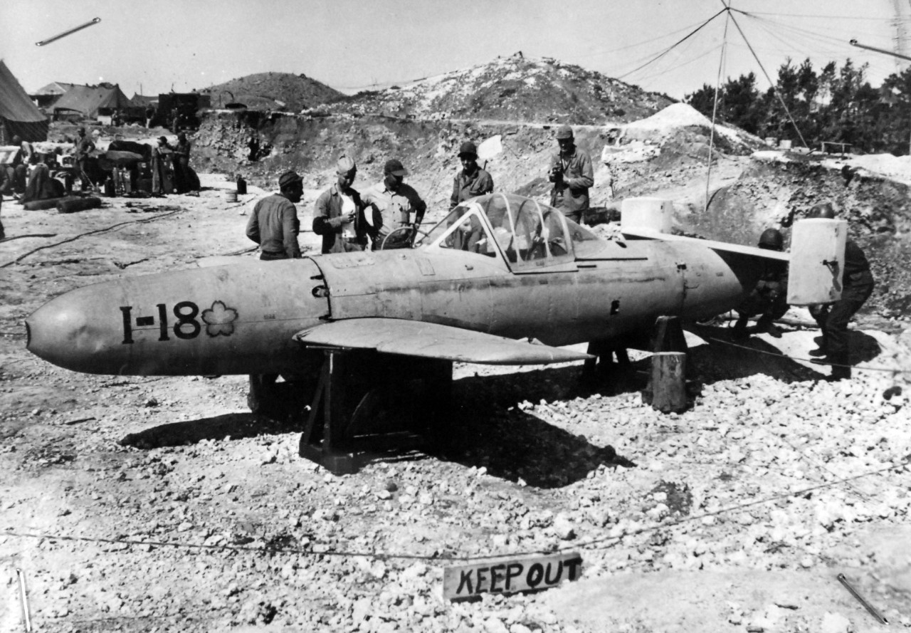 208-MO-Box-113-Okinawa-2:  Okinawa Campaign Yokosuka, MXY7 Ohka, 1945.   U.S. Marines Examine Japanese Suicide Rocket Bomb on Okinawa.  U.S. Marines examine a “Baka Bomber”, Japanese suicide rocket bomb on Okinawa’s Yontan airfield, where several of the craft were abandoned by the enemy when U.S. Tenth Army forces captured the enemy airbase.  The rocket-propelled bomb is steered by a lone pilot who is carried to his death.  Equipped with wings, fins and tail assembly, the craft were named “Baka Bombs” by American Soldiers.  “Baka” means “fool” in Japanese.  A few of the bombs were launched in the Okinawa operation and met with little success.  U.S. Marine Corps Photograph, from the Office of War Information Collection, located at the National Archives.   (2018/05/09).  